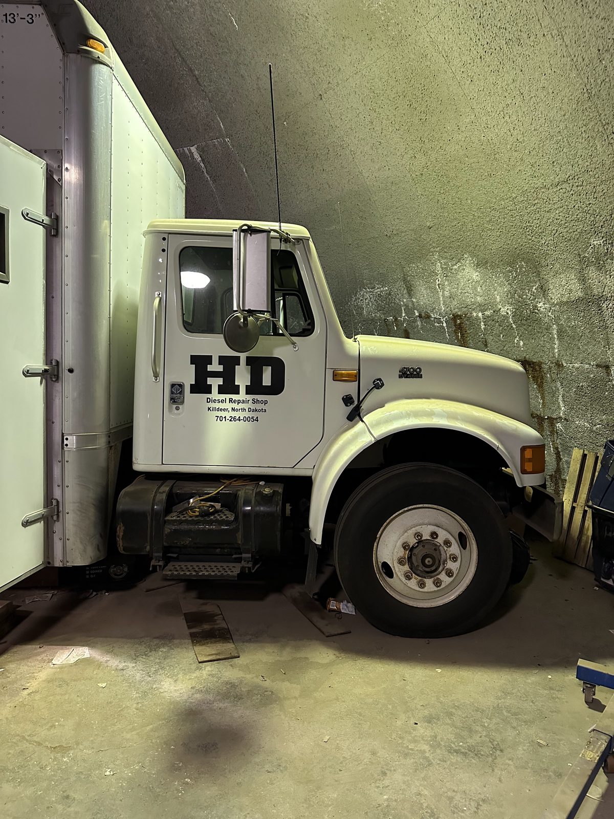 An International service truck lettered for the shop, parked inside a bay with the hood shut and the floor swept