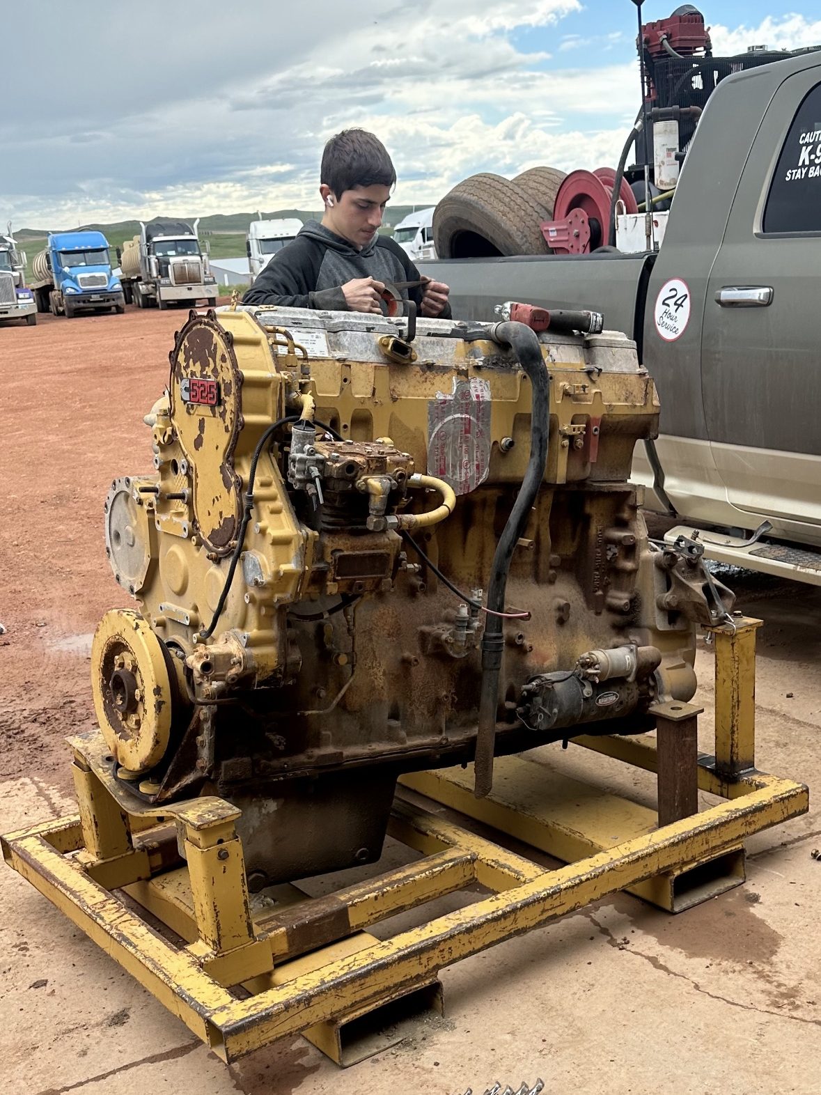 A yellow Caterpillar diesel engine out of the truck and up on a steel stand on the shop lot, part-way through a rebuild