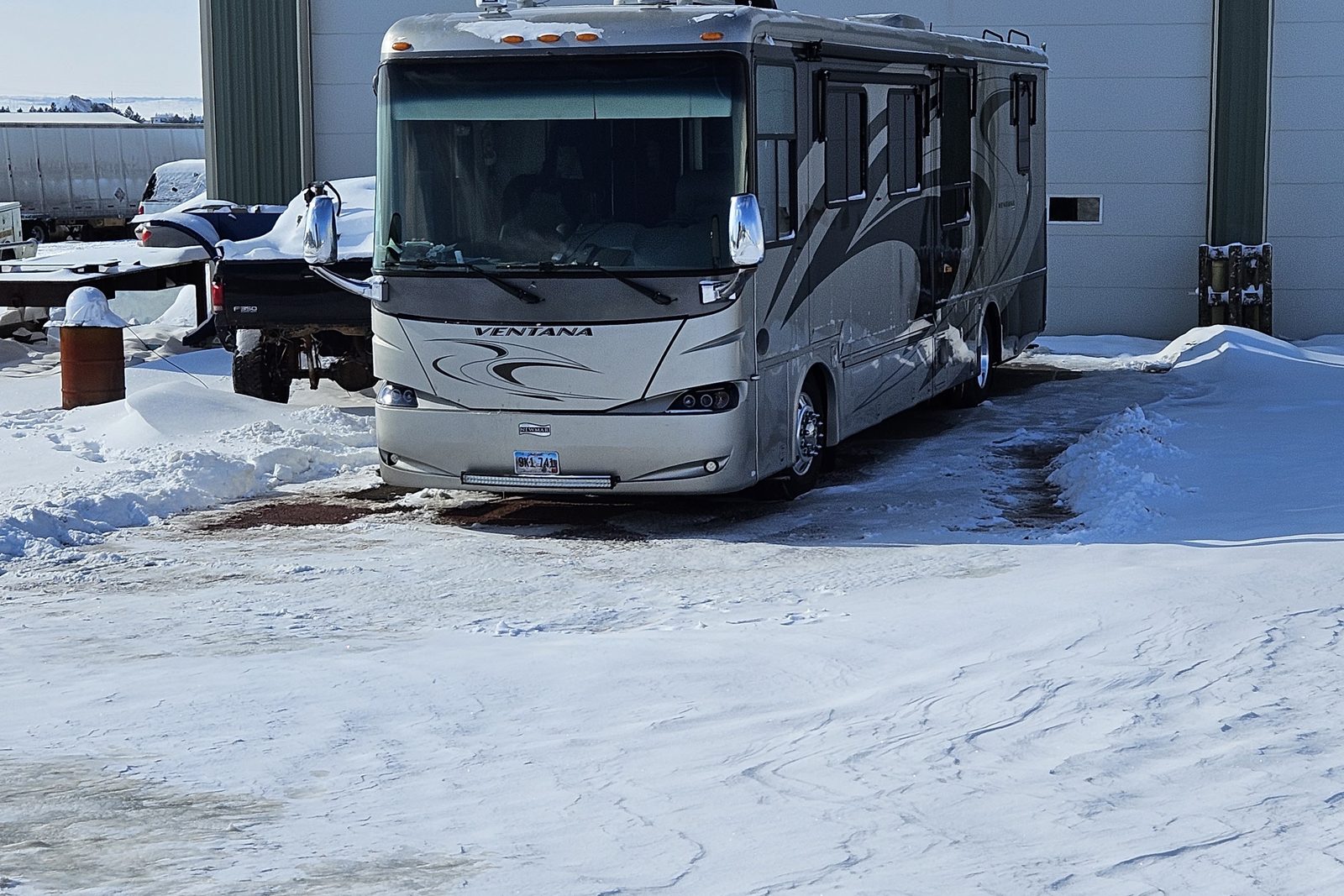 A Class A diesel motorhome parked in the snow beside the shop
