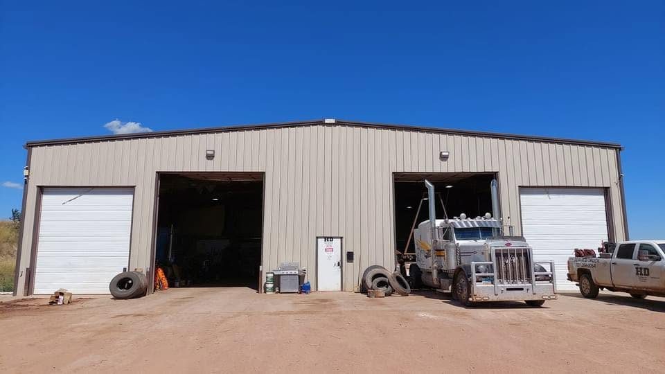 The Killdeer shop with a bay door up and a chrome semi tractor inside, tires stacked outside and an HD pickup at the right
